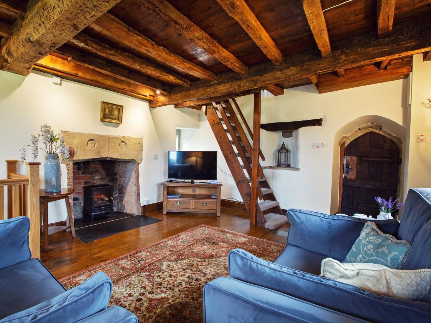 A rustic living room with a fireplace, a television, and a staircase.
