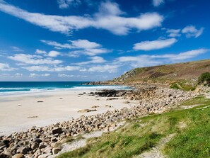 A coastal landscape with a sandy beach, rocky shoreline, and a clear blue sky. - 3 Bed in Penzance (oc-75686) (Lamorna)
