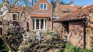 Ein traditionelles Backsteinhaus mit einem Ziegeldach, einer mittleren Tür mit Glasfeldern und einem Garten mit Gartenmöbeln.