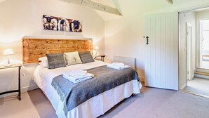 Ein Schlafzimmer mit einem hölzernen Kopfende, einem Bett mit weißer Bettwäsche, einer grauen Decke und einem Gemälde über dem Bett.