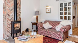 Ein gemütliches Wohnzimmer mit Kamin, einem gemusterten Sofa, einem Holztisch und einer Tür zu einem anderen Raum.
