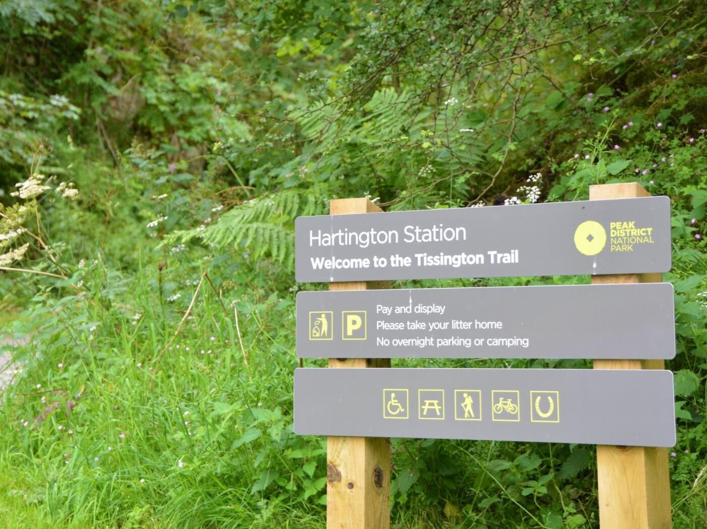 Un panneau d’information indiquant l’emplacement de la gare de Hartington et le tracé du sentier de Tissington, avec des pictogrammes indiquant les zones de stationnement et les points d’accès au sentier.