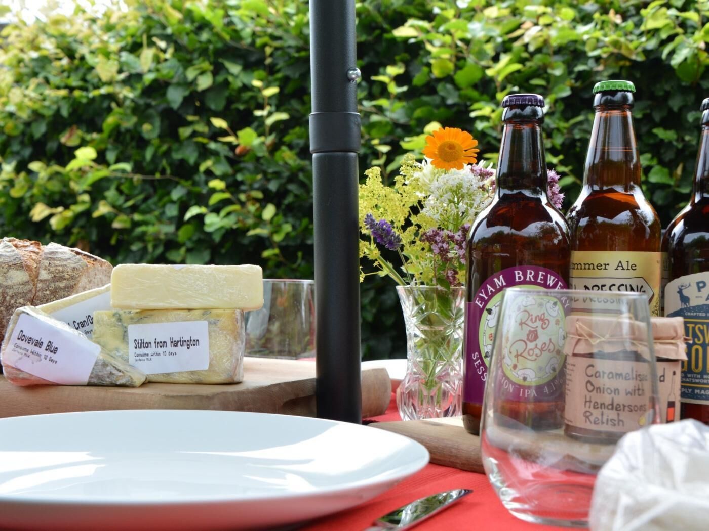 Een tafel met kaas, bierflesjes en een vaas bloemen.