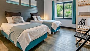 A modern bedroom with two beds, a window with curtains, and a wooden chair. - 3 Bed in Penzance (oc-75635) (Gulval)