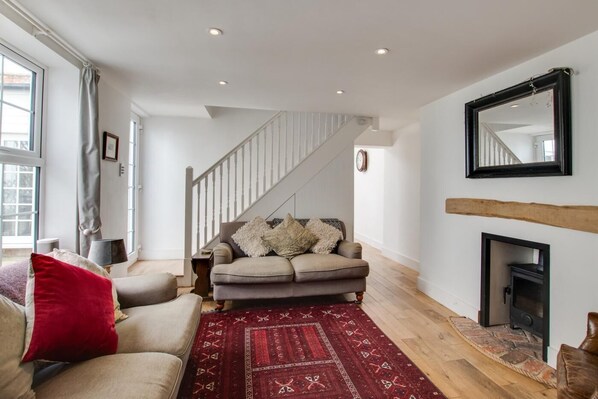 A living room with a sofa, a red rug, a fireplace, and a staircase. - 3 Bed in Folkestone (oc-75607) (Sandgate)