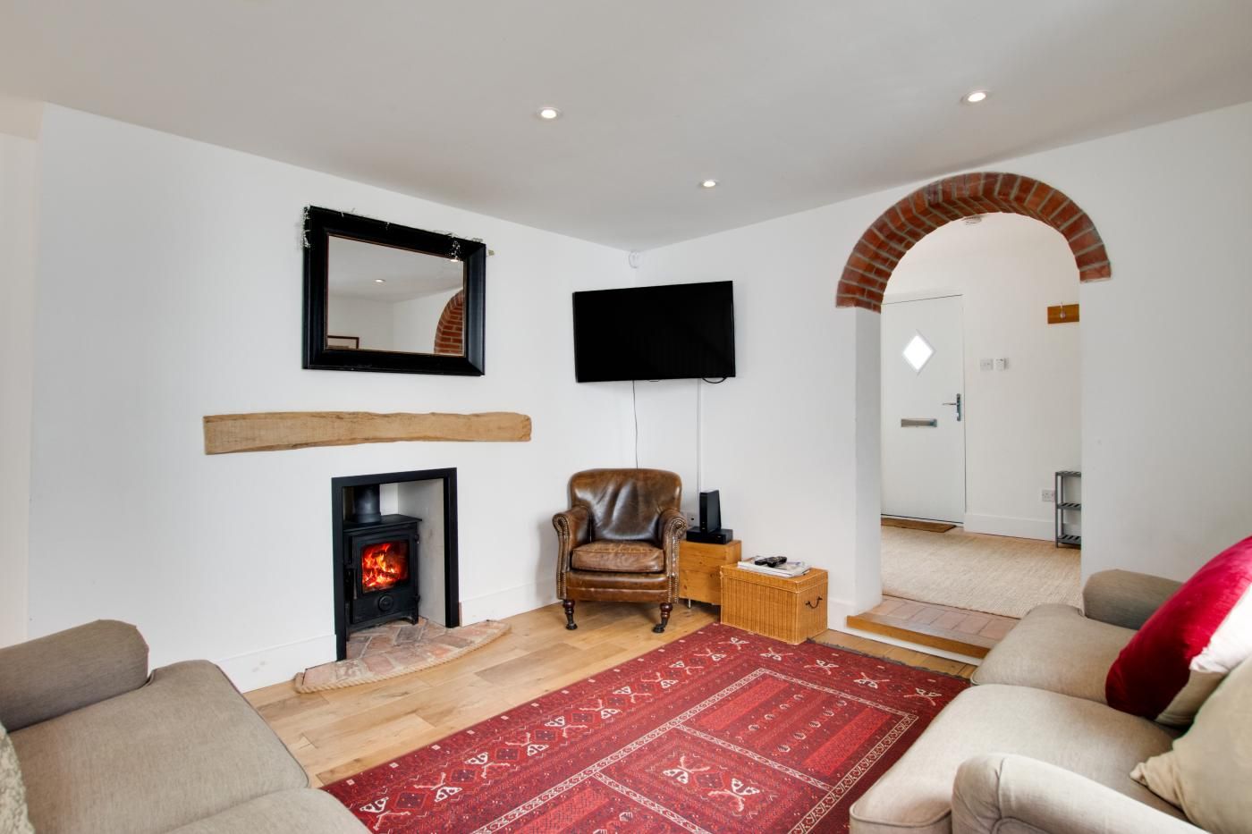 A living room with a fireplace, a leather armchair, a flat-screen TV, and a red patterned rug.