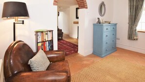 Uma sala de estar com um sofá de couro, uma estante, uma cômoda azul, uma luminária e um tapete vermelho.