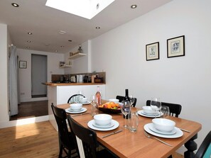 A dining area with a wooden table set for four, white plates, glasses, and a fruit bowl. - 3 Bed in Folkestone (oc-75607) (Sandgate)