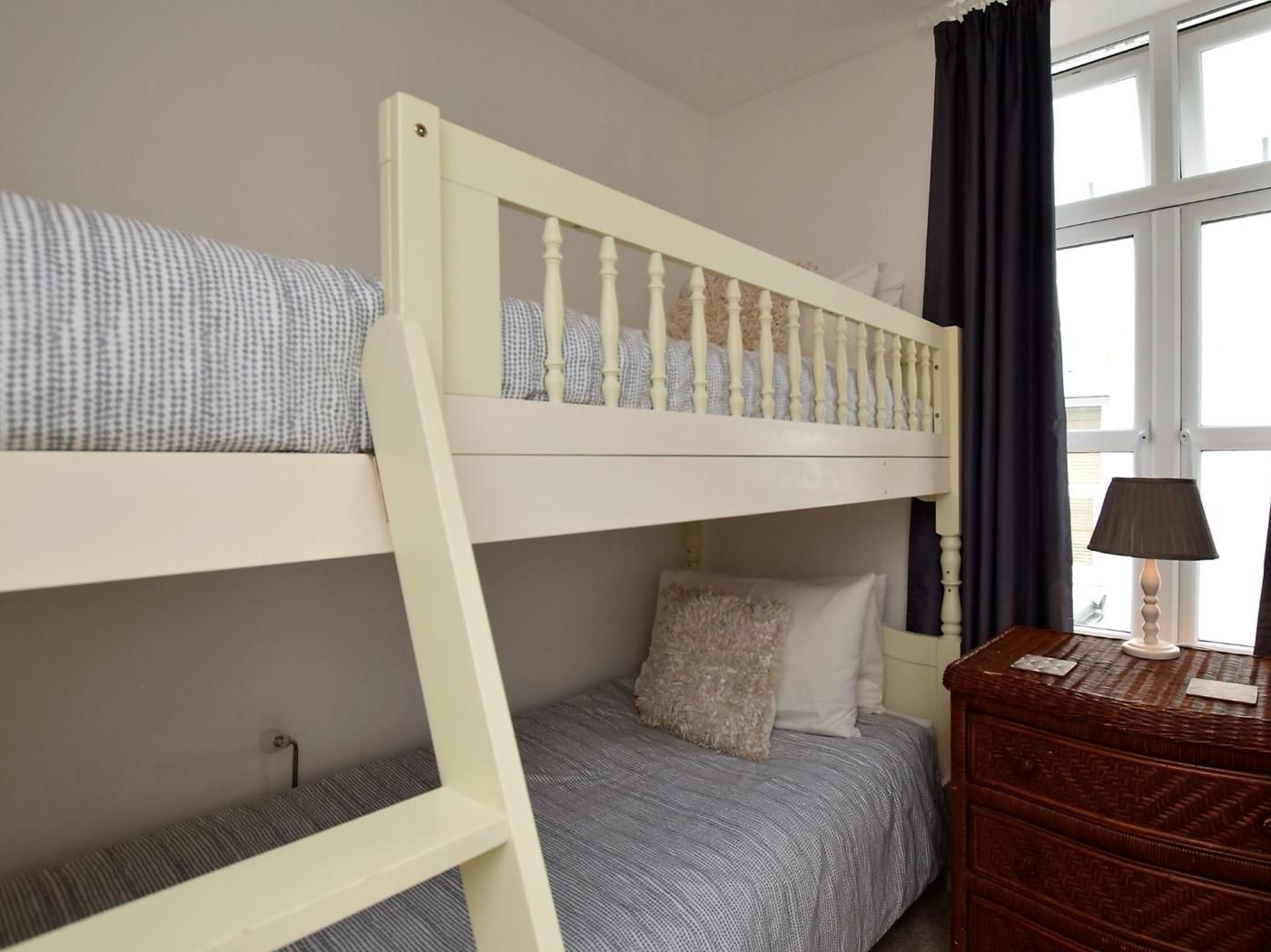 A bunk bed with a ladder, a bedside table with a lamp, and a window with curtains.