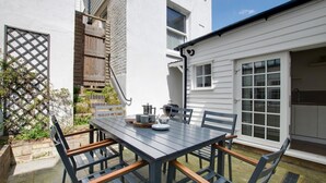Um pátio com mesa, cadeiras, churrasqueira e um prédio branco com porta de garagem.