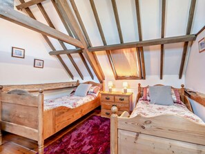 Ein Schlafzimmer mit zwei Holzbetten, einem Schminktisch und einer schrägen Decke mit freiliegenden Balken.