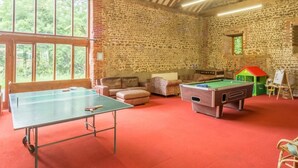 Ein Raum mit Tischtennisplatte, Billardtisch und einer Steinwand.