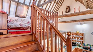 Eine Holztreppe führt zu einem Schlafzimmer mit einem Bett, einer Küchenzeile mit einem Herd und einer gefliesten Spritzschutzwand.