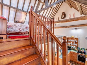 Eine Holztreppe führt zu einem Schlafzimmer mit einem Bett, einer Küchenzeile mit einem Herd und einer gefliesten Spritzschutzwand.
