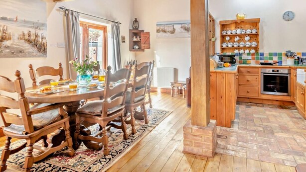 Ein rustikales Interieur mit einem Holzespeisetisch, Stühlen, einer Küchenzeile mit Fliesenrückwand und einem Kamin aus Ziegelsteinen.