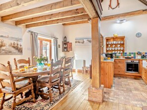 A rustic interior with a wooden dining table, chairs, a kitchen area with a tiled backsplash, and a brick fireplace. - 3 Bed in King's Lynn (oc-75673) (Tattersett)