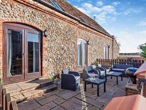 Ein Steinhäuschen mit Terrasse, Gartenmöbeln und einem Grill.