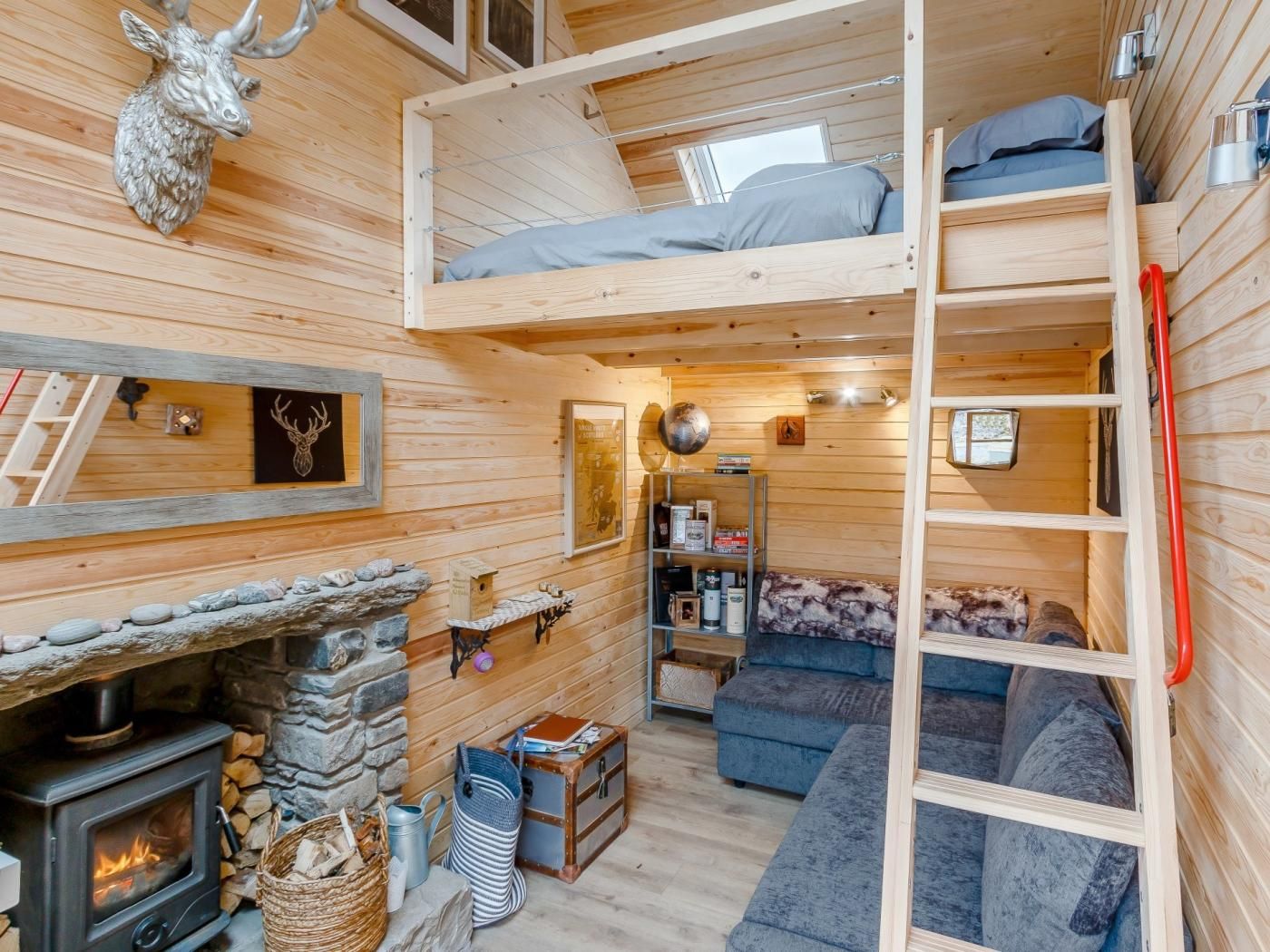 A cozy cabin interior with a loft bed, a fireplace, a sofa, and a ladder.