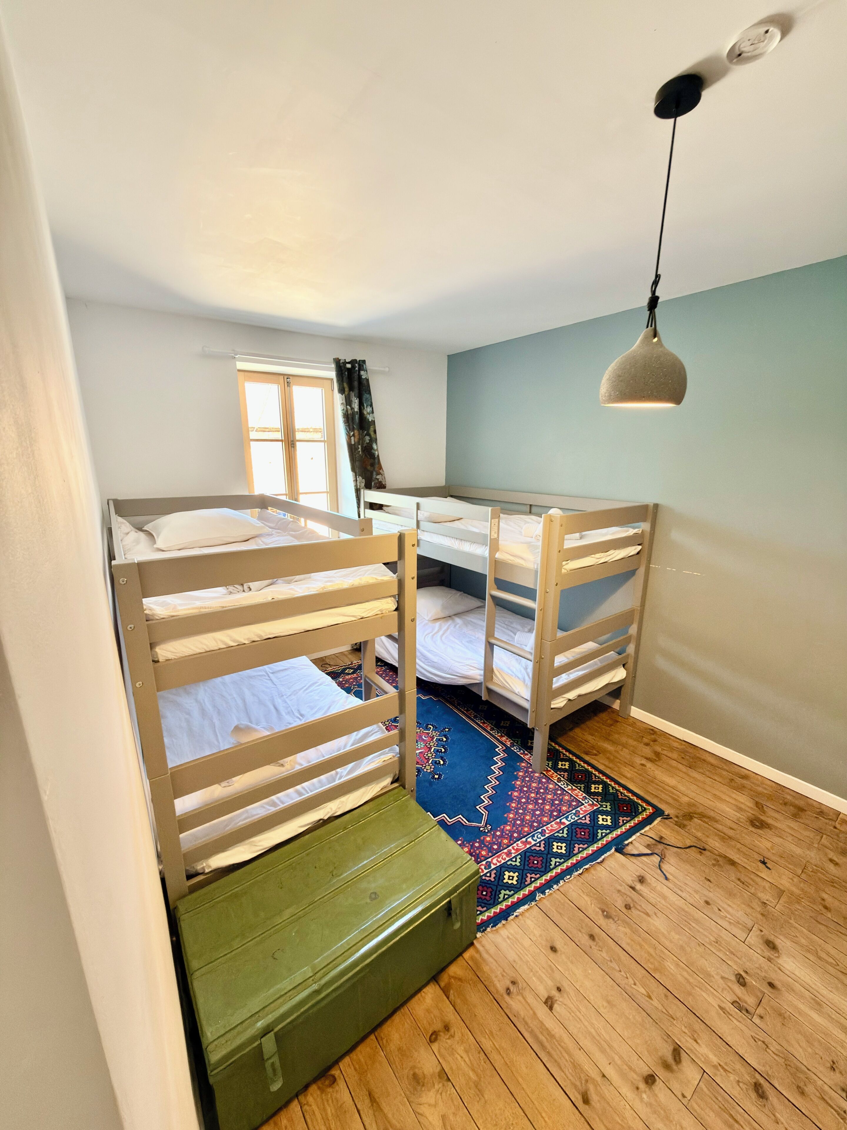 Una habitación con literas, una ventana con cortinas, una lámpara colgante y una alfombra estampada.