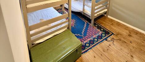 Una habitación con literas, una ventana con cortinas, una lámpara colgante y una alfombra estampada.