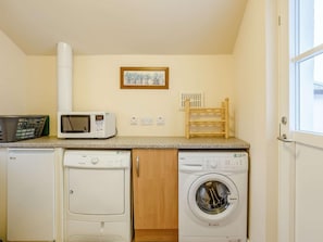 A laundry room with a washing machine, dryer, microwave, and a small wooden rack.