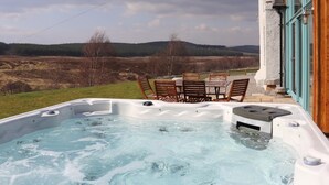 Un bain à remous avec des chaises et une table en bois, le tout entouré d’un paysage magnifique.