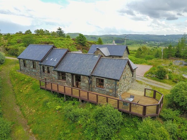 Une maison en pierre dotée d’une terrasse et de nombreuses pièces, entourée de verdure et de collines.