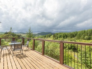 Une terrasse en bois avec une table et des chaises, donnant sur une vallée boisée.