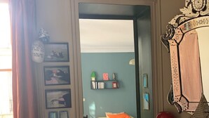 Ein Zimmer mit einem Bett, einem Sessel, einem Spiegel und einer Tür zu einem anderen Raum.