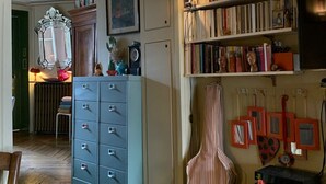 Ein Zimmer mit Bücherregal, Gitarre, Schrank und einem gerahmten Bild an der Wand.