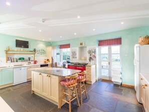 Eine Küche mit einer zentralen Kochinsel, Barhocker, einem eingebauten Backofen und einem Kühlschrank.