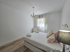 A bedroom with a bed, a chandelier, a nightstand, a lamp, and a window with curtains. - Home, Holidays, Rentals: Eloise Costa, Barcelona. (Pineda de Mar)