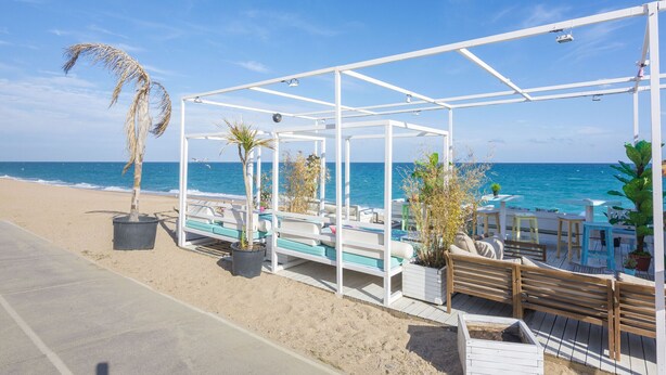 Zona d'estar a l'aire lliure al costat de la platja, amb estructures blanques, plantes en testos i vista a l'oceà.