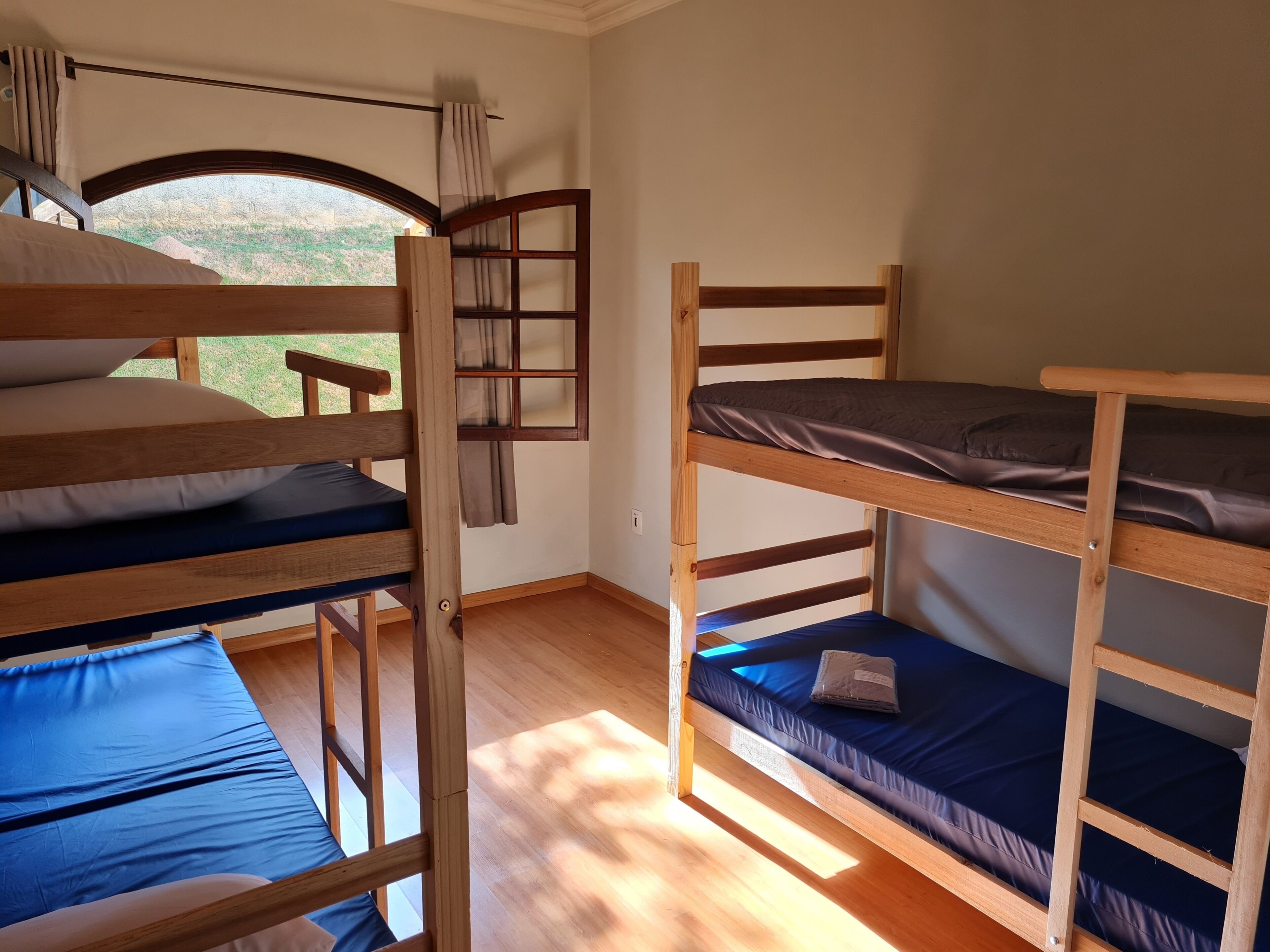A room with bunk beds, a window with curtains, and a view of greenery outside.