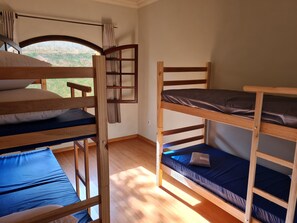 A room with bunk beds, a window with curtains, and a view of greenery outside.