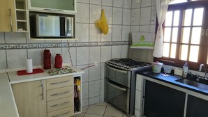A kitchen with a microwave, stove, and sink. There is a window with curtains and a towel hanging on the wall.