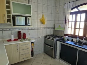 A kitchen with a microwave, stove, and sink. There is a window with curtains and a towel hanging on the wall.