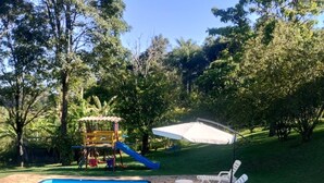 A swimming pool with a stone border, a children's play area, and outdoor seating.