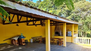 A covered outdoor patio with a brick oven, wooden furniture, and a yellow wall.