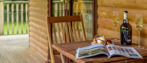 A wooden deck with a wooden chair, a table with a magazine, a bottle of wine, and two glasses.