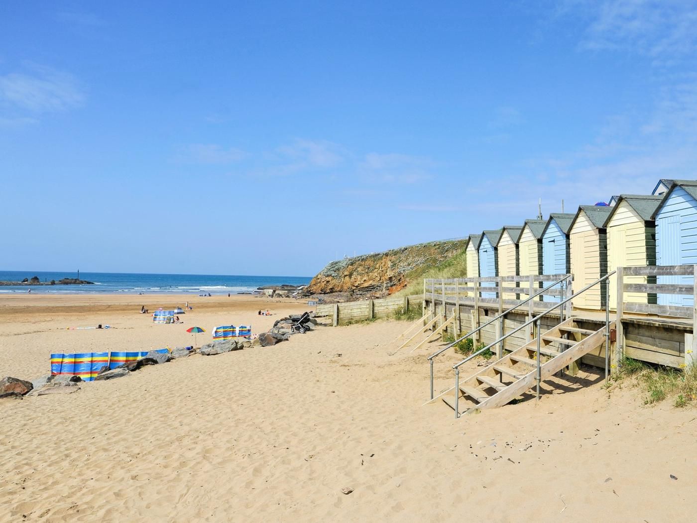 Une plage avec des passerelles en bois menant à des cabanes de plage, une plage de sable et l’océan en arrière-plan.