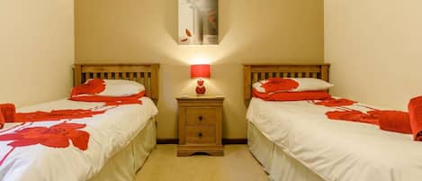 A room with two beds, each with red floral bedding, a nightstand with a lamp, and a painting on the wall.