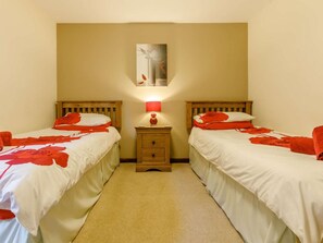 A room with two beds, each with red floral bedding, a nightstand with a lamp, and a painting on the wall.