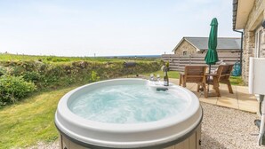 Un bain à remous avec deux coupes de champagne, une table en bois avec des chaises et une maison en pierre avec vue sur la mer.