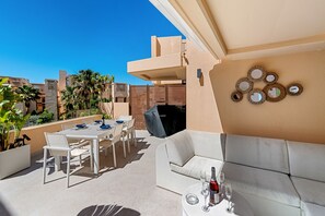 En takterrass med ett matbord, stolar, en soffa och en grill.