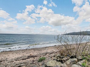 A beach with a rocky shoreline, calm sea, and distant hills. - 3 Bed in Isle Of Arran (oc-ca226) (Whiting Bay)
