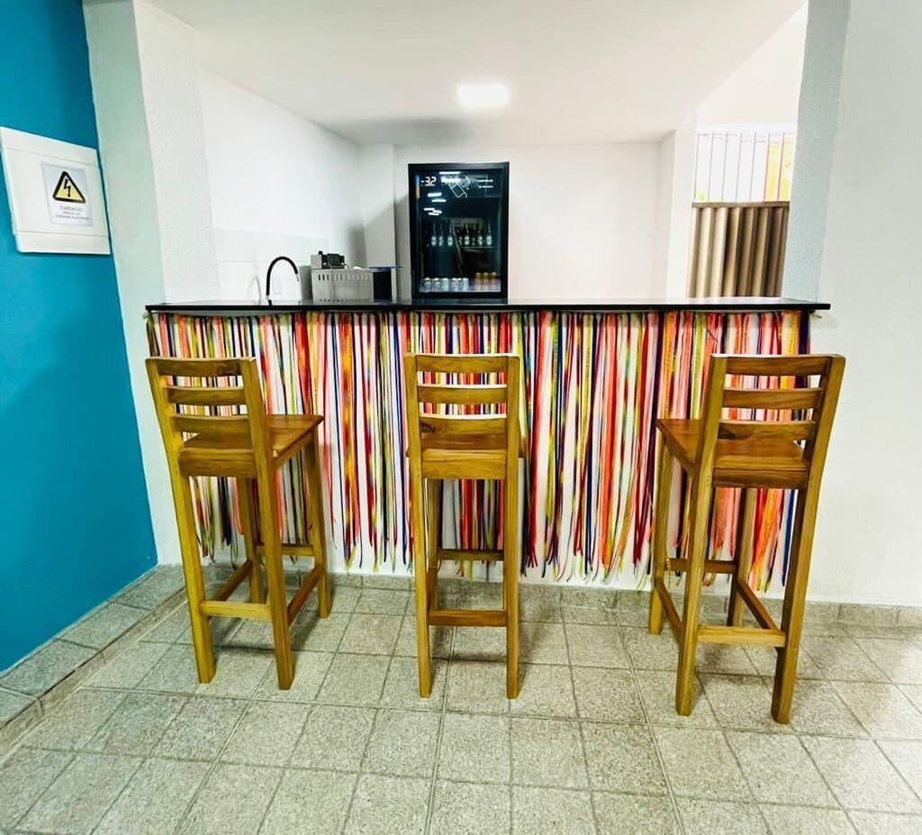 Zona de bar amb tres cadires de fusta, una barra i un frigorífic.