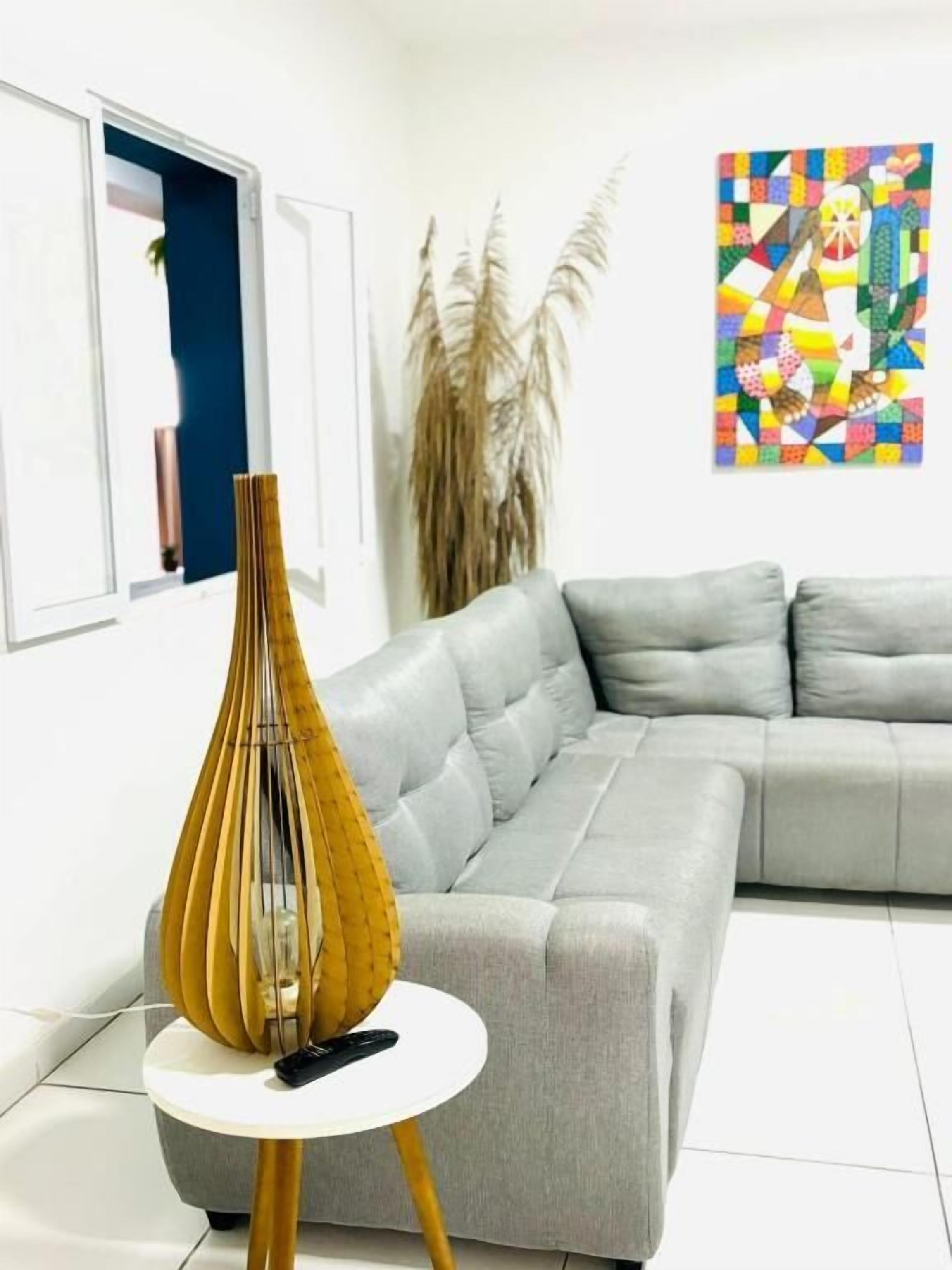 A modern living room with a grey sofa, a round white table with a decorative vase, and a colorful abstract painting on the wall.