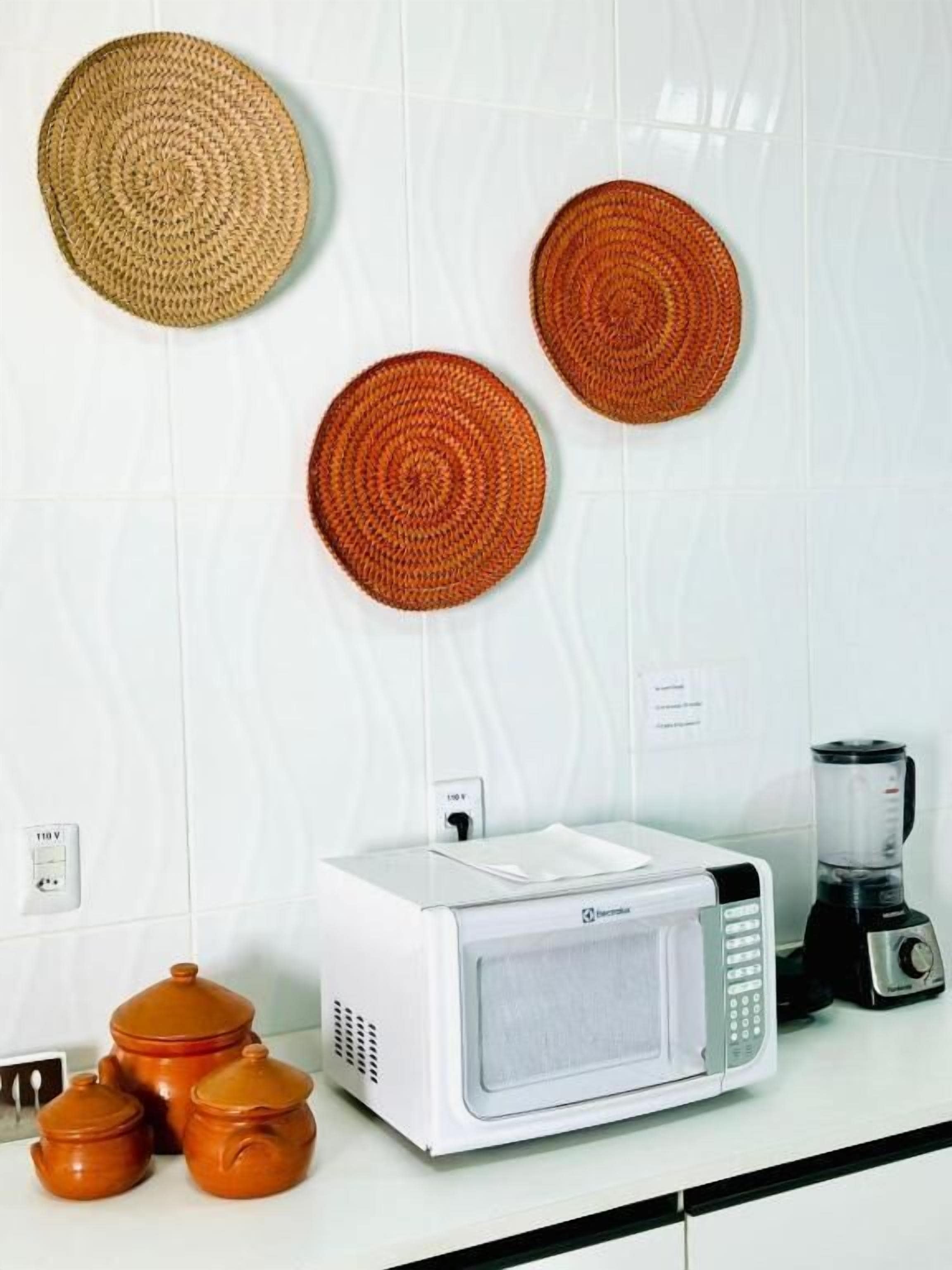 A kitchen with a microwave, blender, and three woven placemats on the wall.