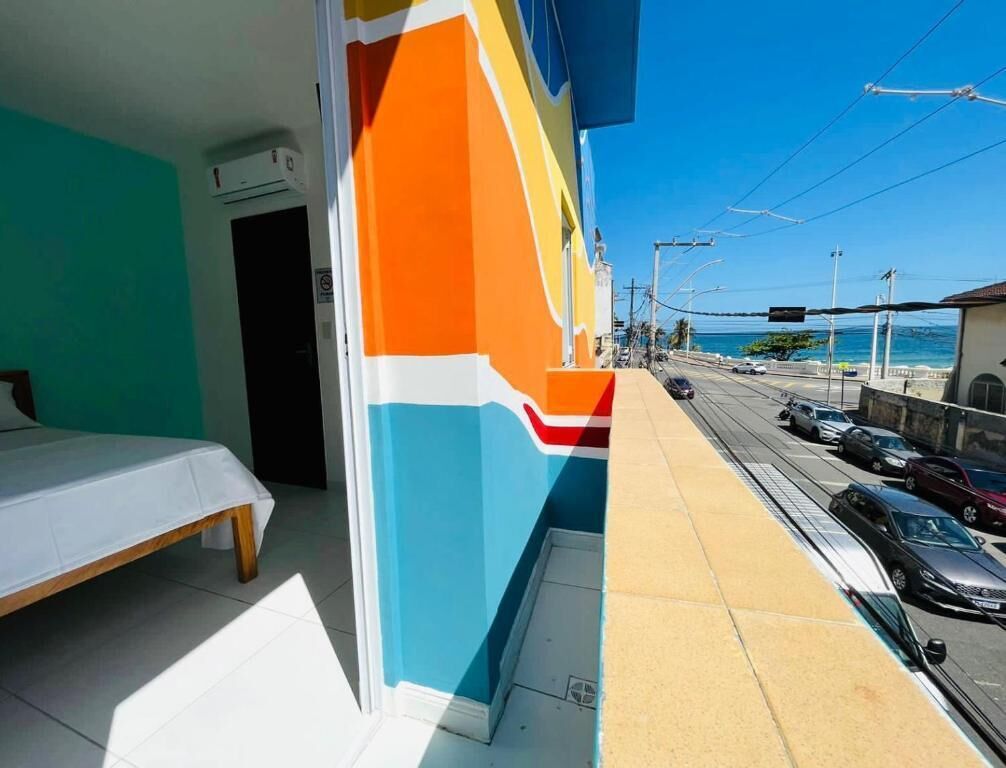 Una habitación con cama y vistas a una calle con coches estacionados y cielo despejado.